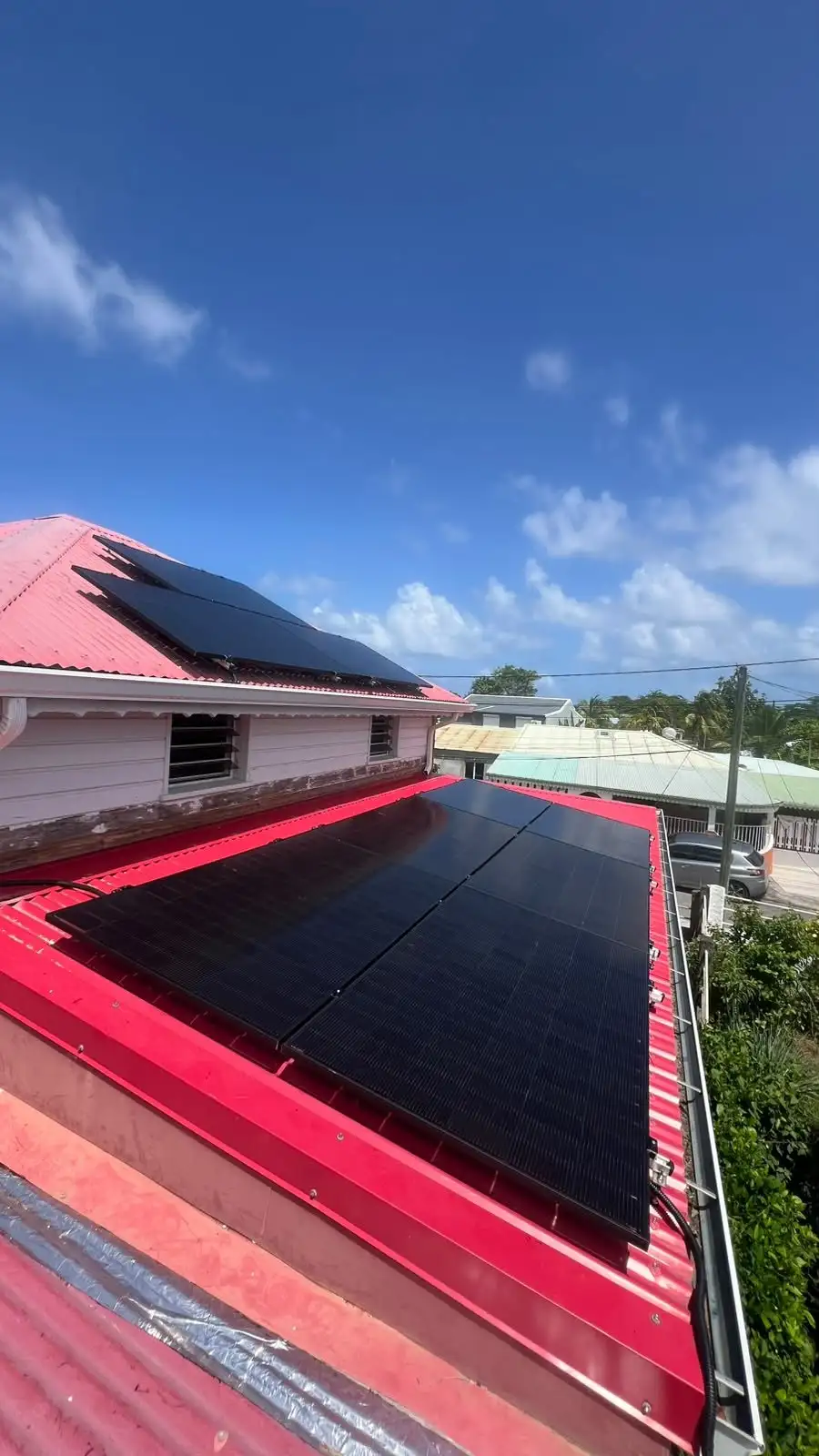 Panneaux solaires noirs posés sur une toiture en tôle rouge en Guadeloupe, sous un ciel bleu